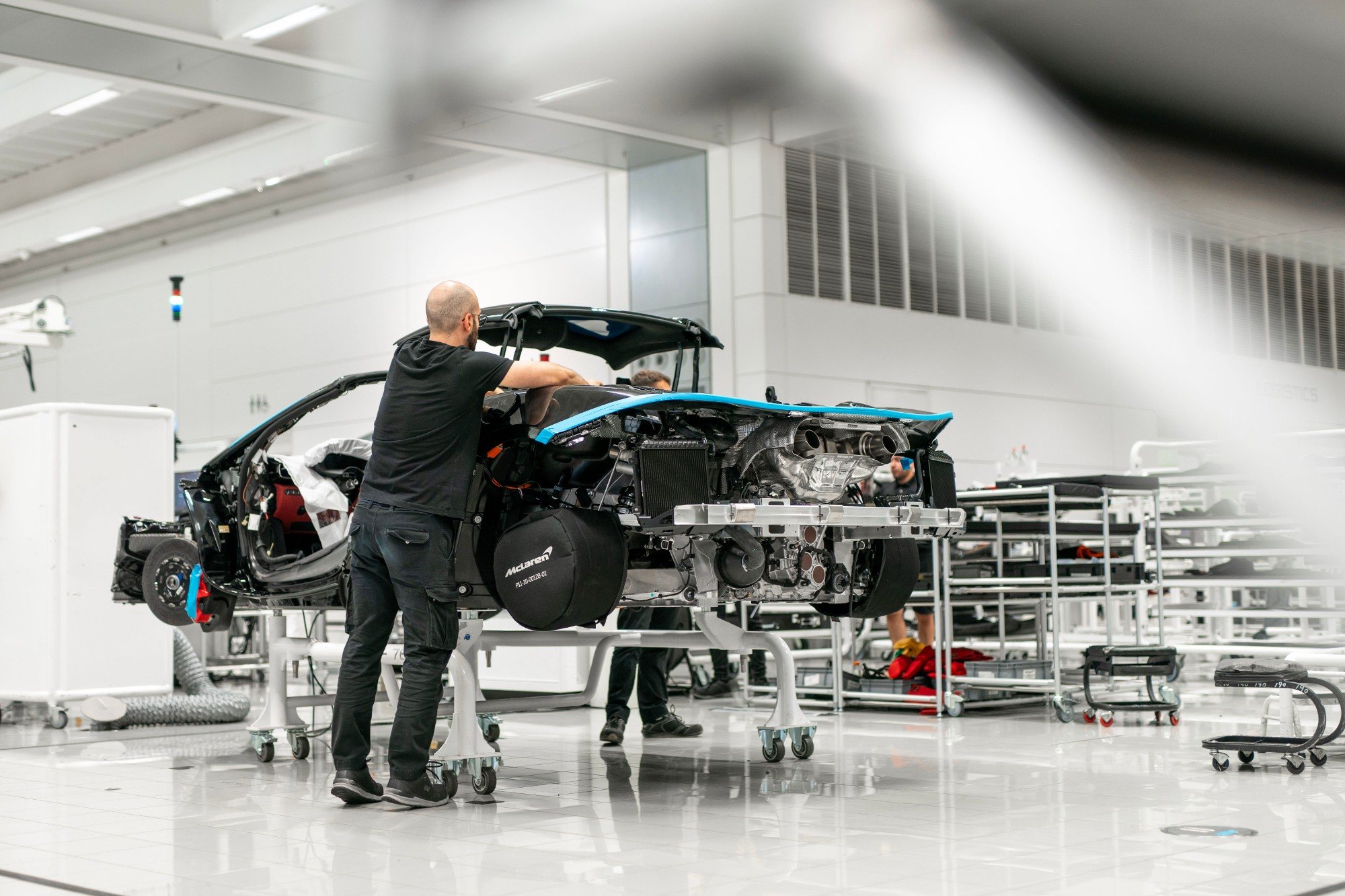 A technician working on a partly assembled McLaren on the production line, with the engine and rear structure exposed