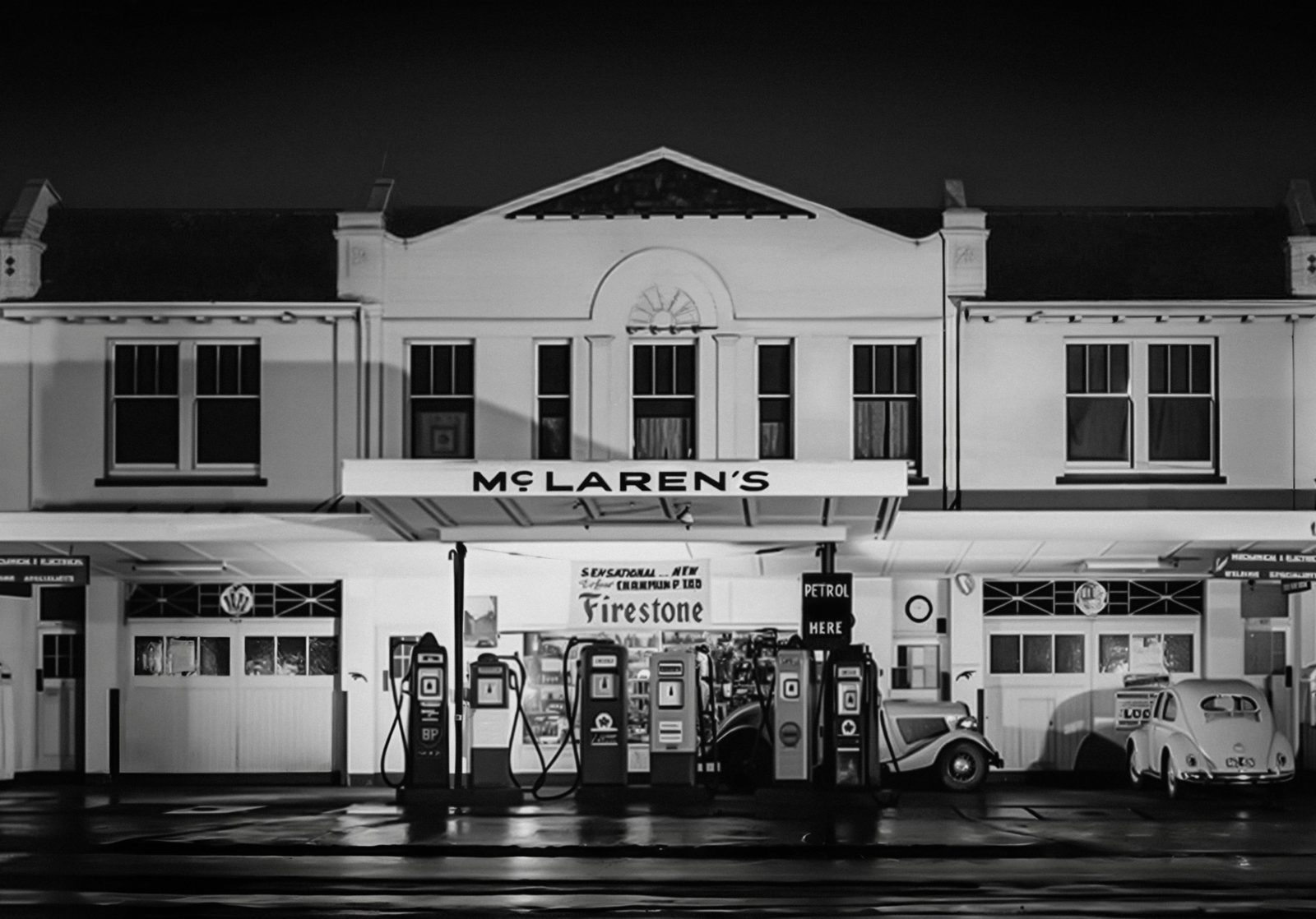 Black-and-white photo of the McLaren family service station at night, with the McLaren’s sign above the petrol pumps