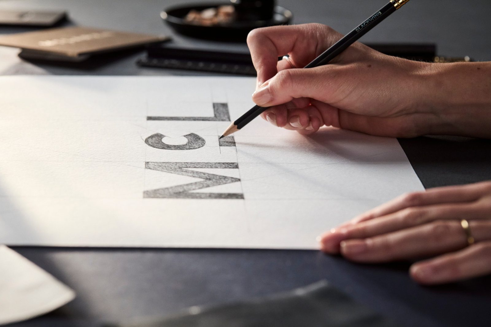 A hand drawing the letters M, c and L of the new McLaren wordmark in pencil, with the small line beneath the c